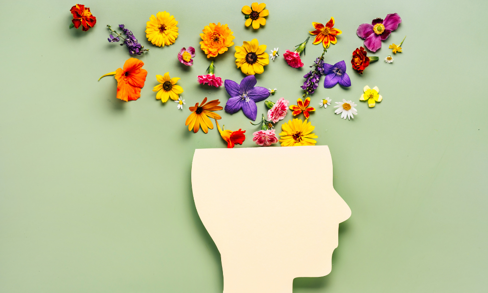 Flowers emerging from the top of a paper cutout resembling the side profile of a person, representing the idea of mental wellness
